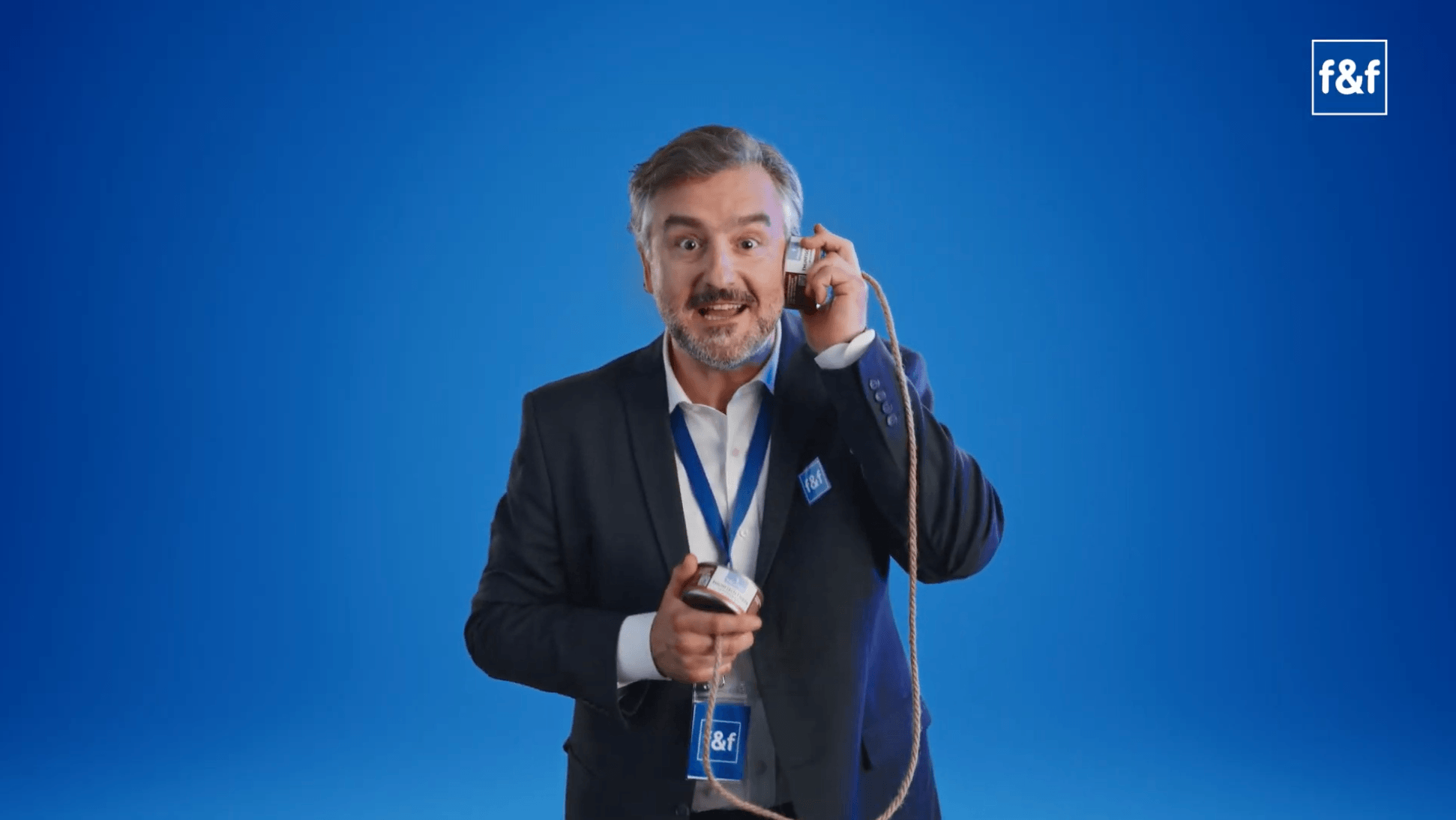 Ein Presenter im dunklen Sakko vor blauem Hintergrund telefoniert mit einer Konservendose an einer Schnur