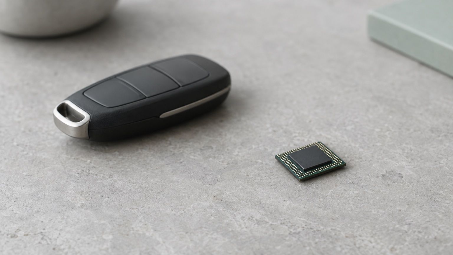 Symbolbild: Autoschlüssel ohne Emblem neben einem Computerchip auf einer Steinplatte