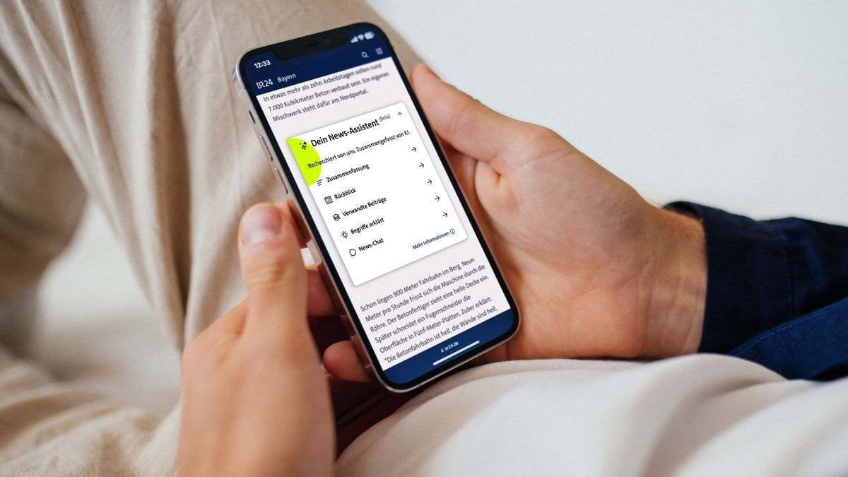 Hände halten ein Smartphone, auf dem BR24 das Menü von „Dein News-Assistent“ zeigt