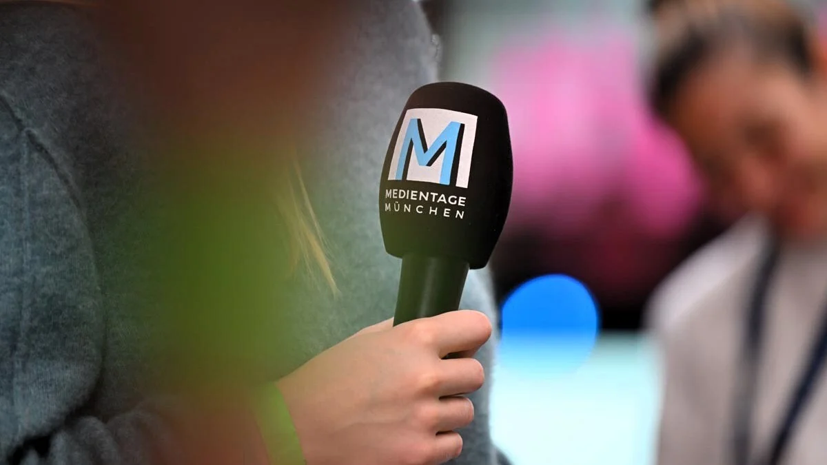 Mikrofon mit dem Logo der Medientage München in einer Hand, Hintergrund unscharf