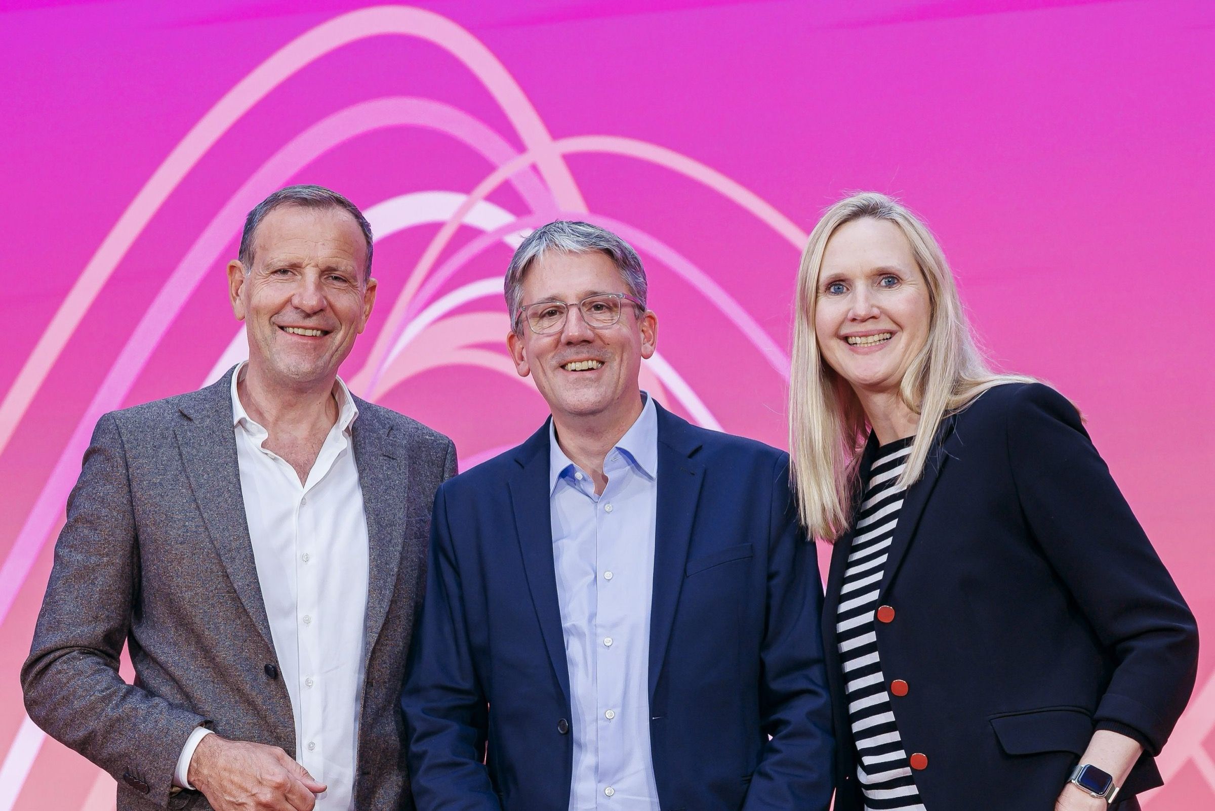 Drei Mitglieder der VAUNET-Vorstandsspitze stehen vor einer pinkfarbenen Wand